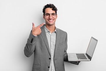 Wall Mural - hispanic handsome man smiling confidently pointing to own broad smile. business and laptop concept