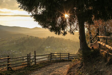 Sunny Warm Picture Of The Village In Mountains, Rural Landscape, Wooden Handmade Fence, Beautiful Sunset Time, Sunbeams Through Pine Tree Branches 