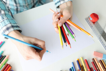 Woman designer drawing with multicolored pencils on paper closeup