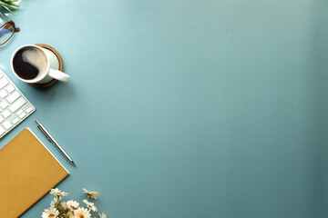Wall Mural - Stylish workplace with wireless keyboard, coffee cup and notebook on blue background.