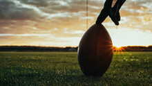 American Football Kickoff Game Start. Close-up Shot Of An American Ball Standing On A Grass Field Held By Professional Player. Preparation For Championship Game.
