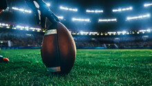 American Football Kickoff Game Start. Close-up Shot Of An American Ball Standing On A Stadium Field Held By Professional Player. Preparation For Championship Game.