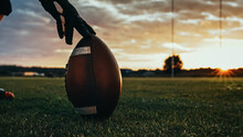 American Football Kickoff Game Start. Close-up Shot Of An American Ball Standing On A Grass Field Held By Professional Player. Preparation For Championship Game.