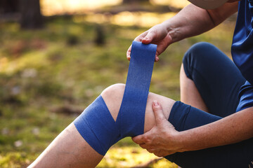 first aid after hiking accident. injured hiker putting elastic bandage to her knee. tendon problems 