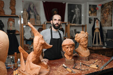 Serious Carpenter At Table With Carved Sculptures