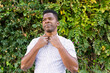 © ADDICTIVE STOCK - Black man buttoning shirt near hedge