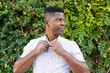 © ADDICTIVE STOCK - Black man buttoning shirt near hedge
