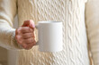 © Anna Fedorova - female hand holding white mug with blank copy space scree for your advertising text message or promotional content, sweet coffee or tea. Girl in beige sweater holding white porcelain mug mock up