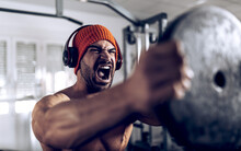 Furious Ethnic Male Athlete Raising Barbell Disc In Gym