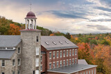 Beautiful sky and colorful autumn scene in historic town of Harrisville, New Hampshire. Old bell tower and preserved textile mill buildings built of granite and brick in 19th century.