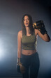 © qunica.com - Photo of a confident young sporty girl with boxing gloves posing over a smokey background