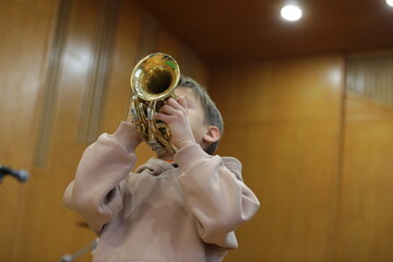 Wall Mural - Portrait of a child playing the trumpet in the room. Student studying music with musical instrument in class.Youth learning and education concept