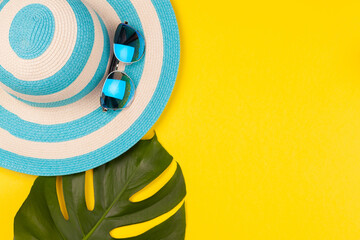 Wall Mural - Top view on beach accessories on yellow background - sunglasses, striped blue hat and monstera leaf. Concept of the long-awaited vacation at sea and travel. Advertising space