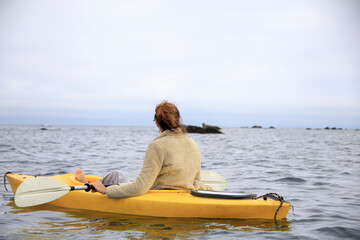 Wall Mural - Woman kayaking in a yellow kayak around rocks in the ocean