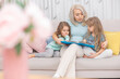 © галина шарапова - Caucasian mom reading a book to children sitting on the sofa in the living room