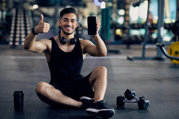 Aufkleber - Cool Fitness App. Young Arab Man Posing In Gym With Blank Smartphone