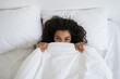 © brizmaker - Afro american woman hides under soft white blanket