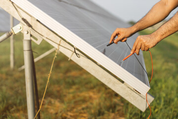 Close up of male hands checking voltage in solar panels with multimeter outdoors. Competente energy technician controlling work of solar station.