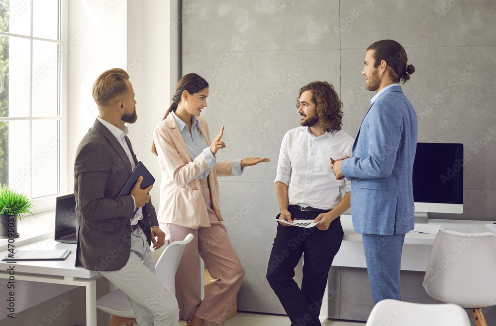 Group of young people standing in the office, having a work meeting and discussing a new business strategy. Female manager talking to a team of male employees or colleagues