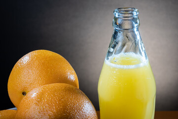 Closeup of moist oranges and glass bottle of orange juice on the table.