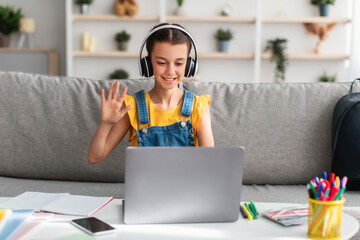 Poster - Cheerful schoolgirl sitting at table, using laptop, waving to pc