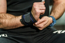 Close Up On Hands Of Unknown Man Holding And Putting On And Adjusting Wrap Bandages On Wrists For Powerlifting Body Building Training Sport Equipment At The Gym