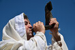 Portrait of an orthodox adult Jewish man blow Shofar (ram's horn) outdoors under clear blue sky, on the Jewish High Holidays in Rosh Hashanah and Yom Kippur.