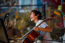 A Laughing Child Sits Outside In Golden Light With A Cello