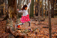 A Little Girl Leaps Of Fallen Tree Into Pile Of Leaves In Autumn