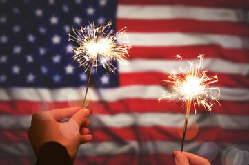 4th of July - Independence Day of USA. Women holding burning sparklers against American flag, closeup