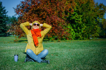 Wall Mural - Carefree hipster woman with raised hands sitting on green lawn enjoying good weather. Outdoor coffee break. Happy lifestyle concept.