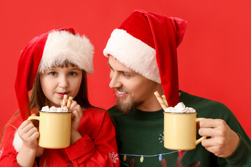 Wall Mural - Happy daughter and father with cups of hot cocoa on color background