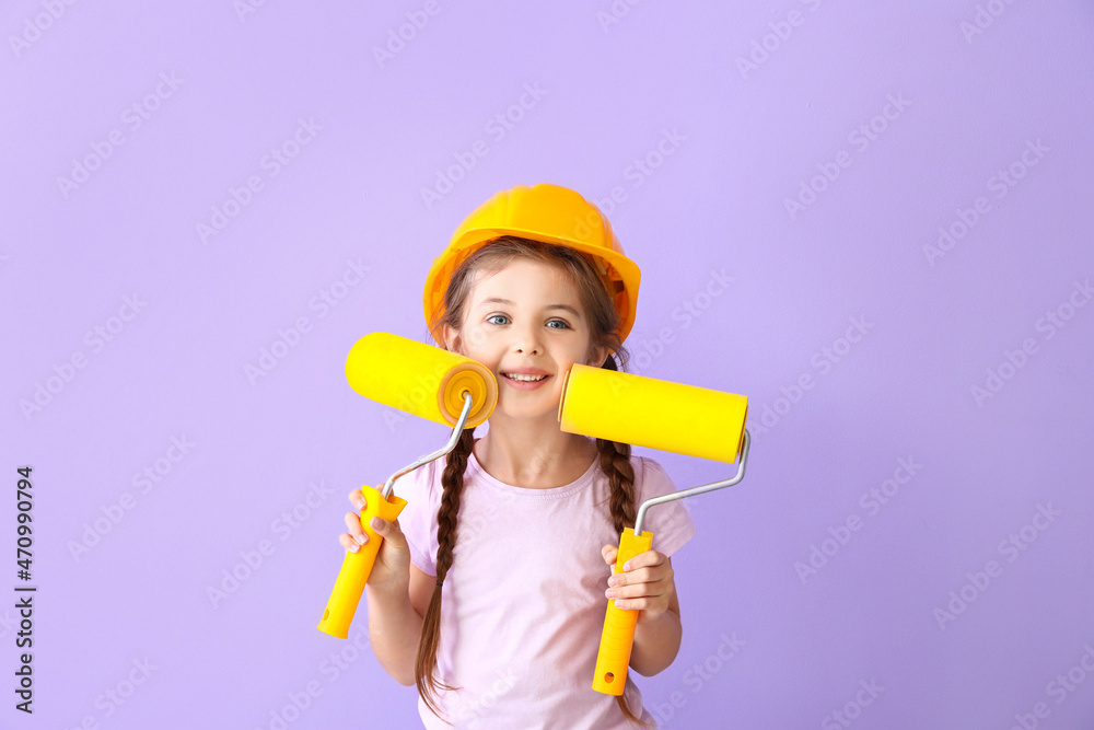 Cute little girl with paint rollers on lilac background