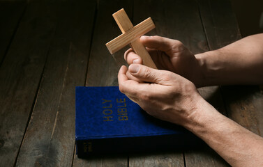 Man with cross and Holy Bible at dark wooden table, closeup