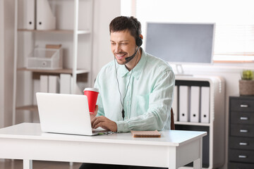 Poster - Consultant of call center with headset with cup of coffee working at table in office