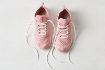 Pair of sportive shoes with untied laces on light wooden background