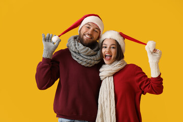 Wall Mural - Happy young couple in stylish winter clothes and Santa Claus hats on color background