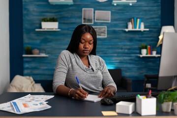Poster - African american woman taking notes on textbook paper using pen to write information at desk with computer. Person writing on notebook file to help with business project, working from home