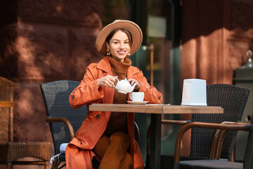 Wall Mural - Beautiful young woman pouring tea from teapot in street cafe