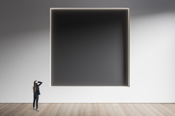Poster - Businesswoman standing in minimalistic concrete and wooden interior with abstract clean black square frame on wall. Mock up. Exhibition, gallery and art concept.