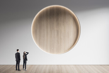 Wall Mural - Businesspeople standing in minimalistic concrete and wooden interior with abstract clean round poster on wall. Mock up. Exhibition, gallery and art concept.