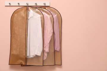 Wall Mural - Garment bags with clothes hanging on light wall. Space for text