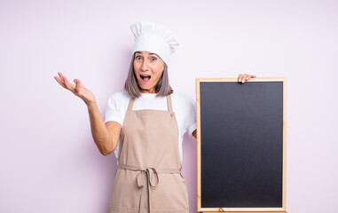 Wall Mural - senior pretty woman feeling extremely shocked and surprised. chef and blackboard concept