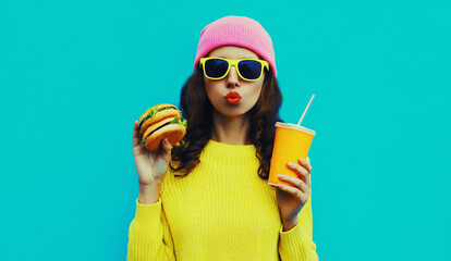 Wall Mural - Portrait of stylish young woman with burger and cup of juice fast food on blue colorful background