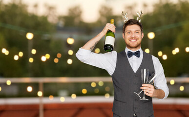 Sticker - celebration, people and holidays concept - happy man with bottle of champagne and wine glasses at christmas or new year party over lights on roof top background