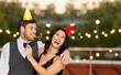 © Syda Productions - birthday, celebration and holidays concept - happy couple with party blowers and caps having fun at rooftop party over lights on background