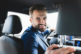 Fototapeta  - Taxi driver smiling while turning over to the backseat looking talking with clients. Successful businessman husband looking at the backseat at dealer shop before buying a car