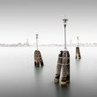 Drei Lampen am Ufer der Lagunenstadt Venedig, Italien, mit der Skyline Venedis im Hintergrund.