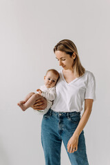 mother holding her baby with one arm, on white wall background.