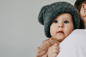 portrait of a baby wearing a gray oversized knitted beanie, on white wall background.